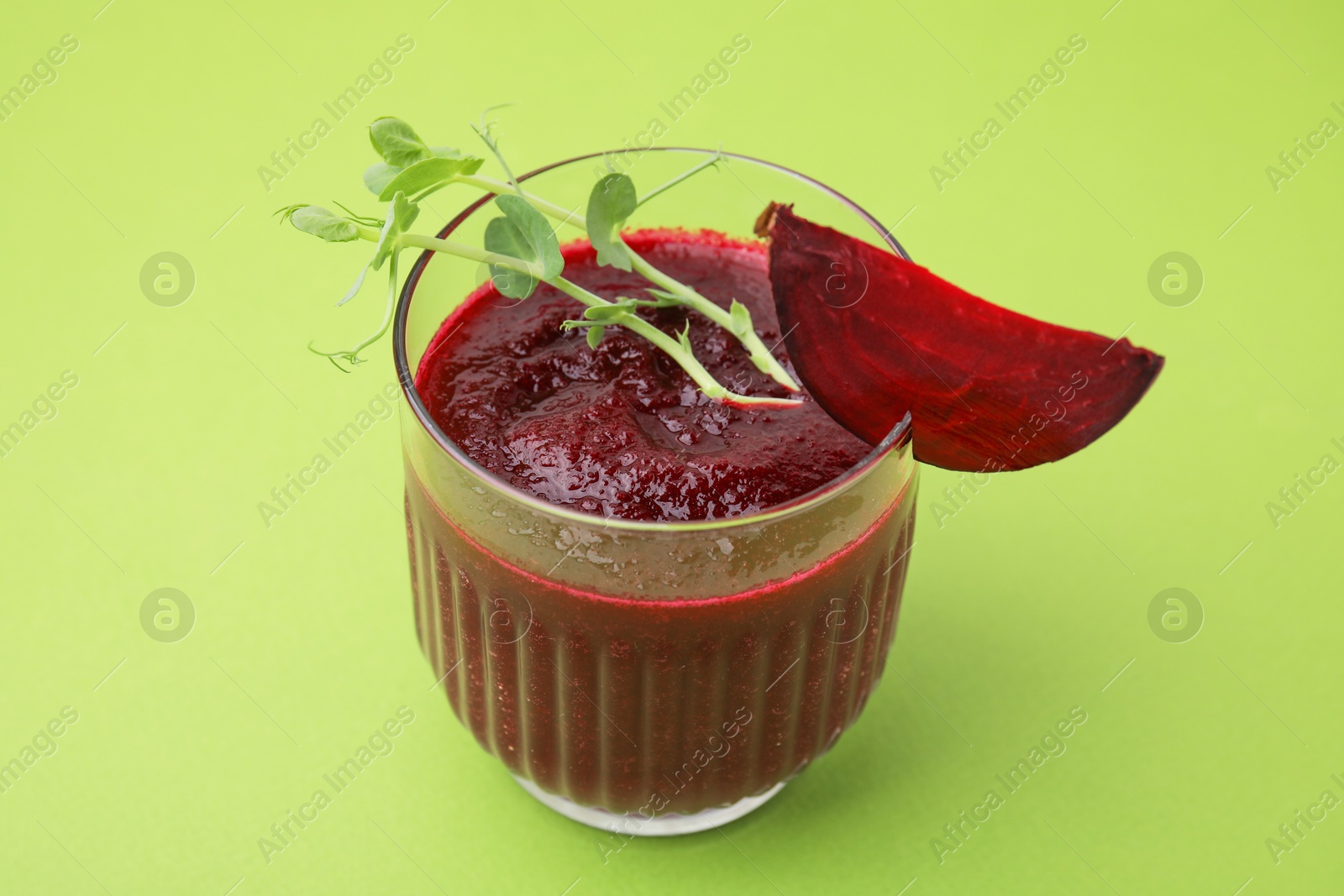 Photo of Tasty beetroot smoothie with microgreens in glass on green table, closeup. Vegan drink