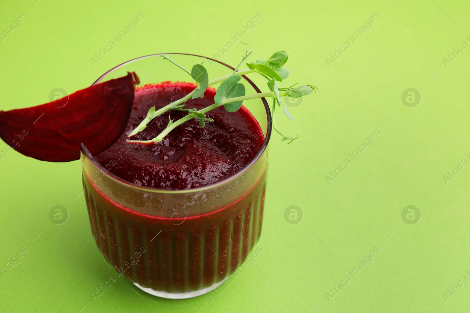 Photo of Vegan drink. Tasty beetroot smoothie with microgreens in glass on green table, closeup. Space for text