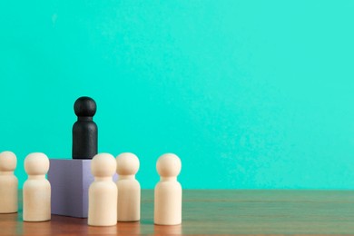 Photo of Black piece among wooden ones on table against turquoise background, space for text