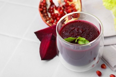 Fresh beetroot smoothie with mint in glass on white tiled table. Space for text