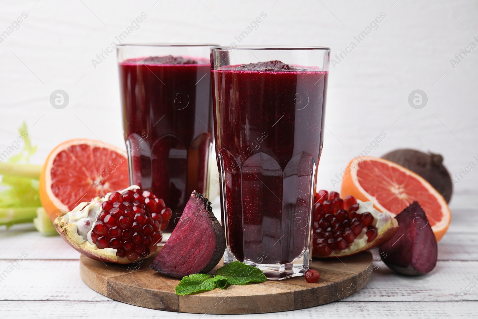 Photo of Fresh beetroot smoothie in glasses, grapefruit, beet and pomegranate on white wooden table