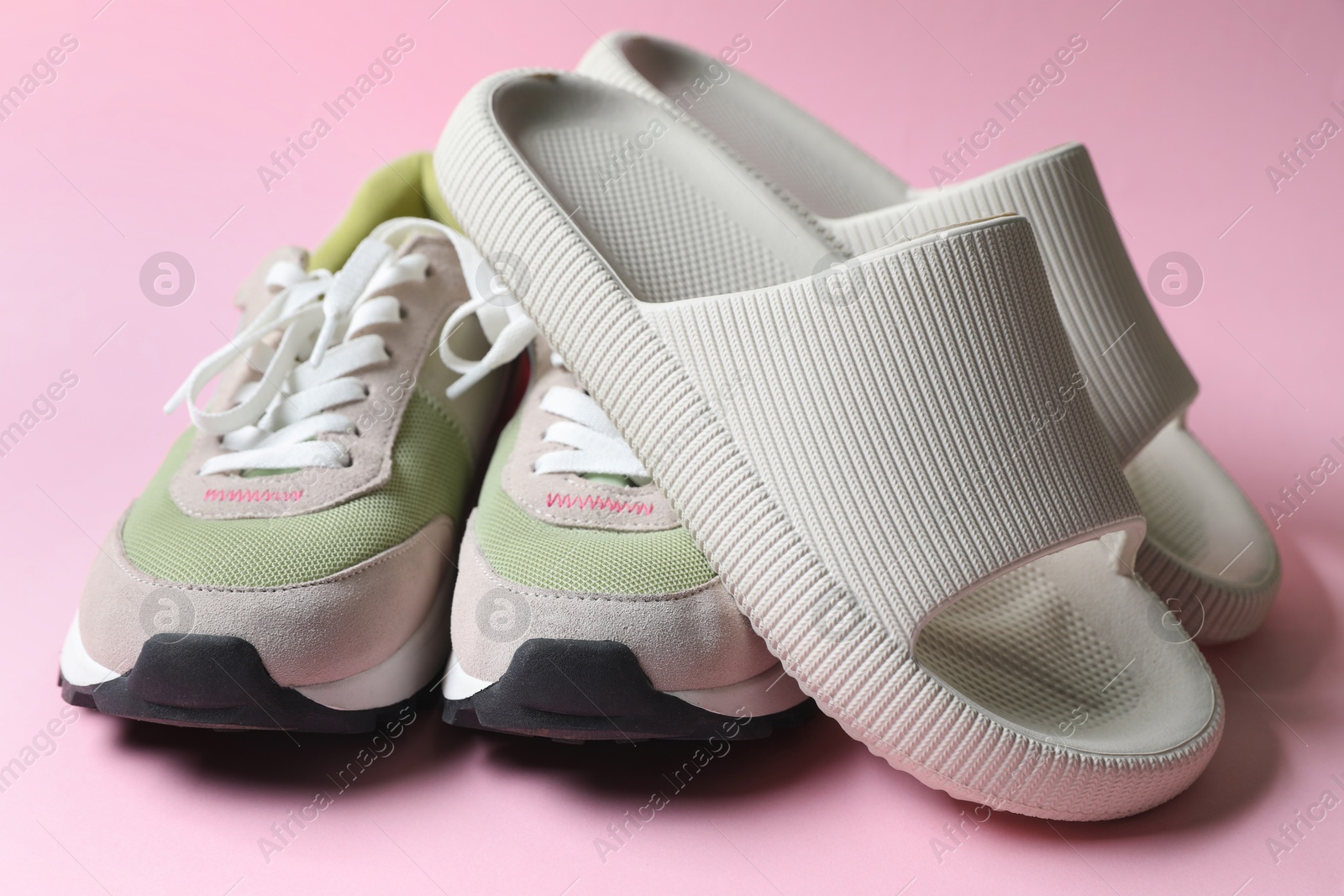 Photo of Rubber slippers and sneakers on pink background, closeup