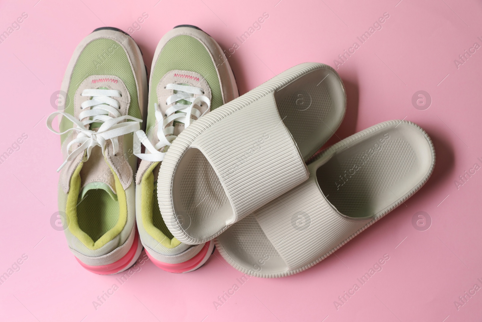 Photo of Rubber slippers and sneakers on pink background, top view