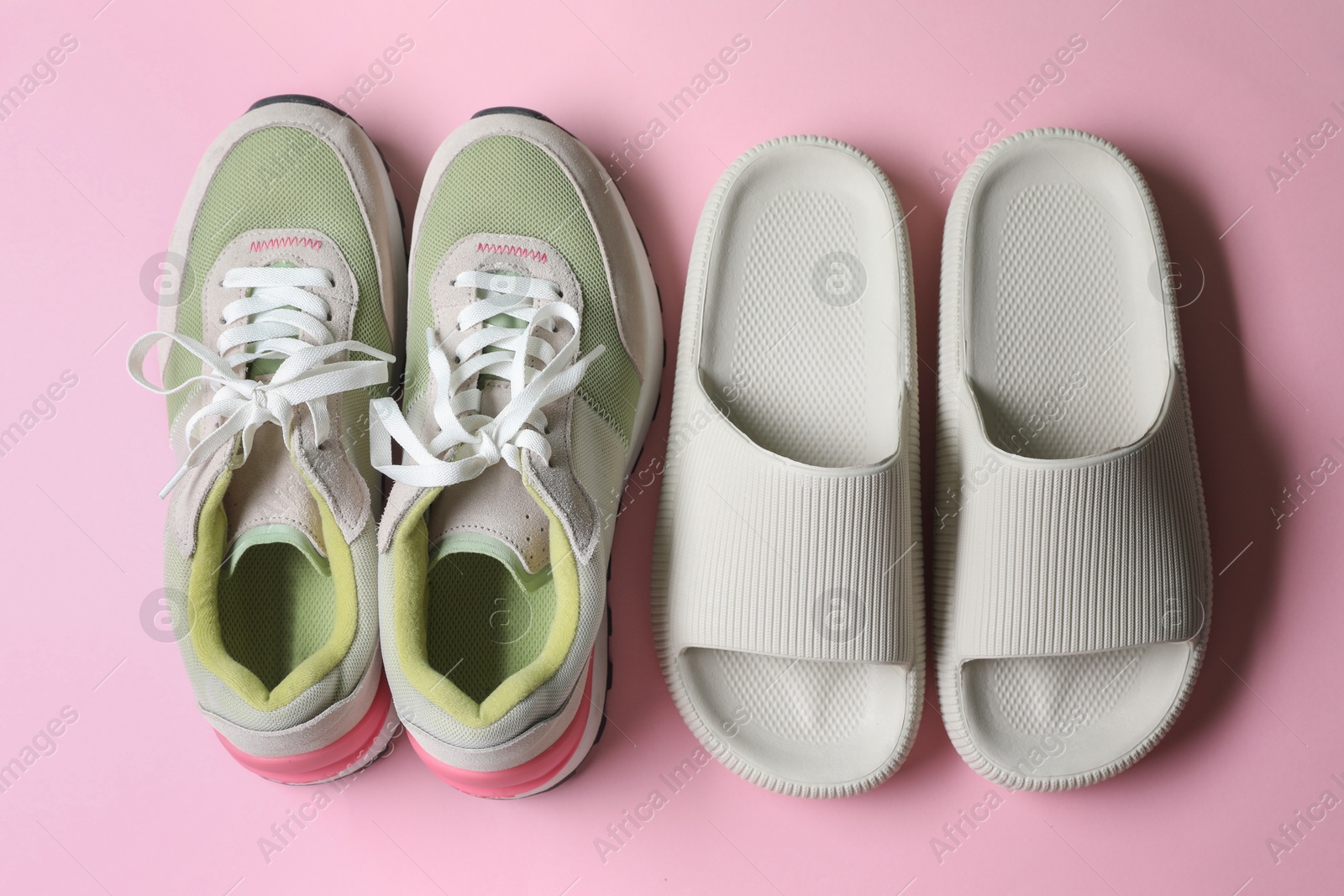 Photo of Rubber slippers and sneakers on pink background, top view