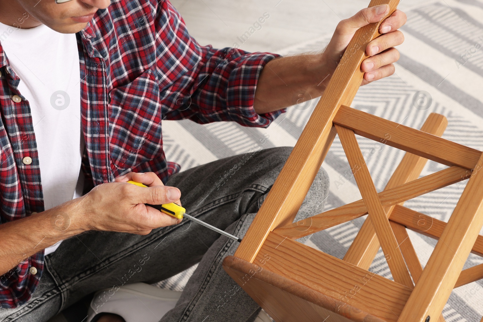 Photo of Man repairing wooden stool with screwdriver indoors, closeup