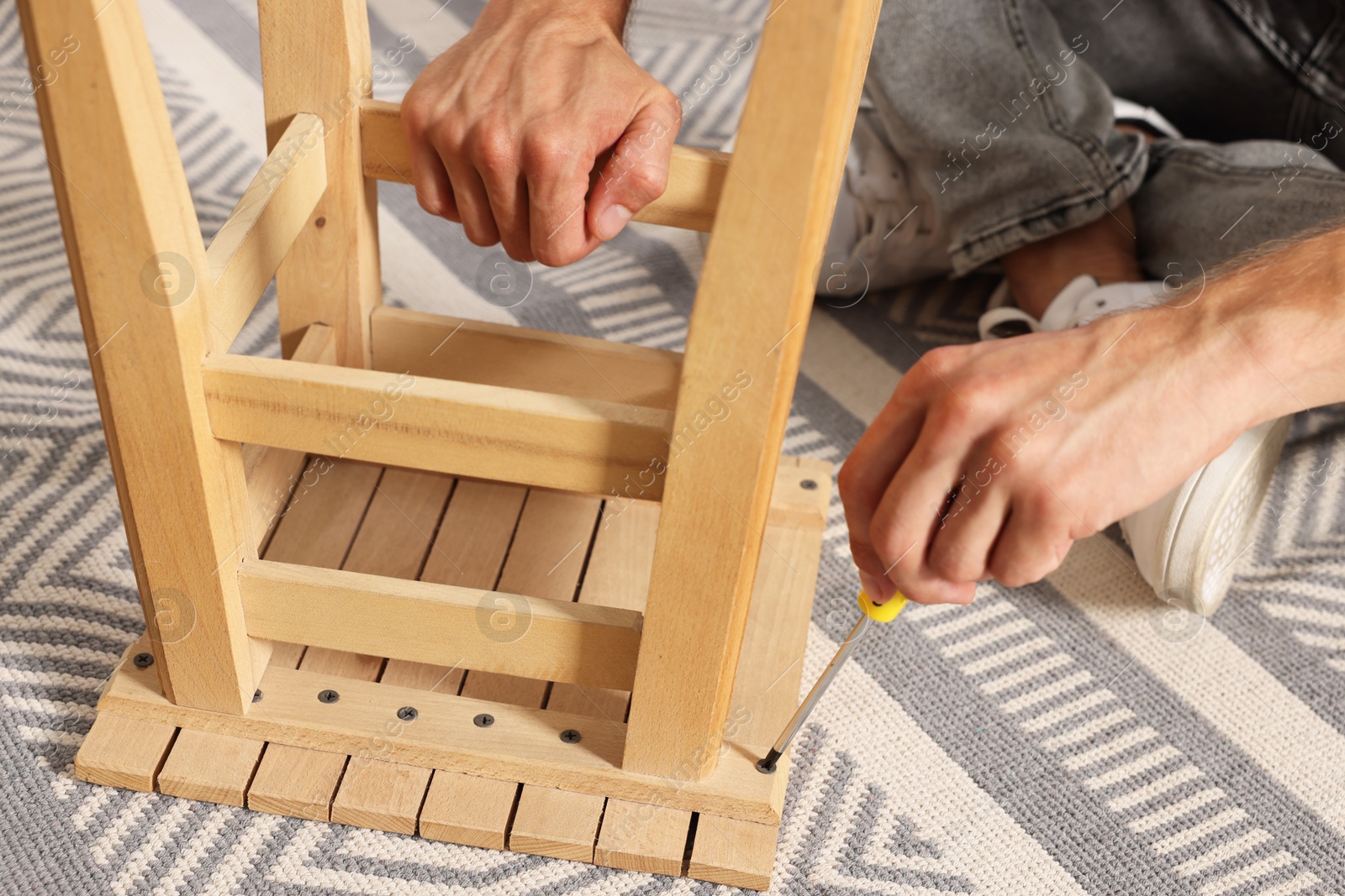 Photo of Man repairing wooden stool with screwdriver indoors, closeup