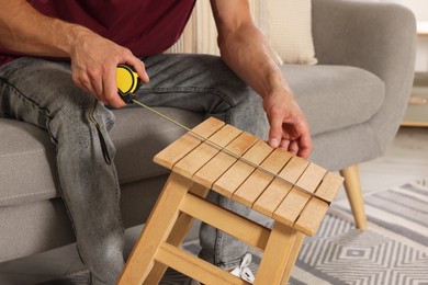 Man using tape measure while repairing wooden stool indoors, closeup