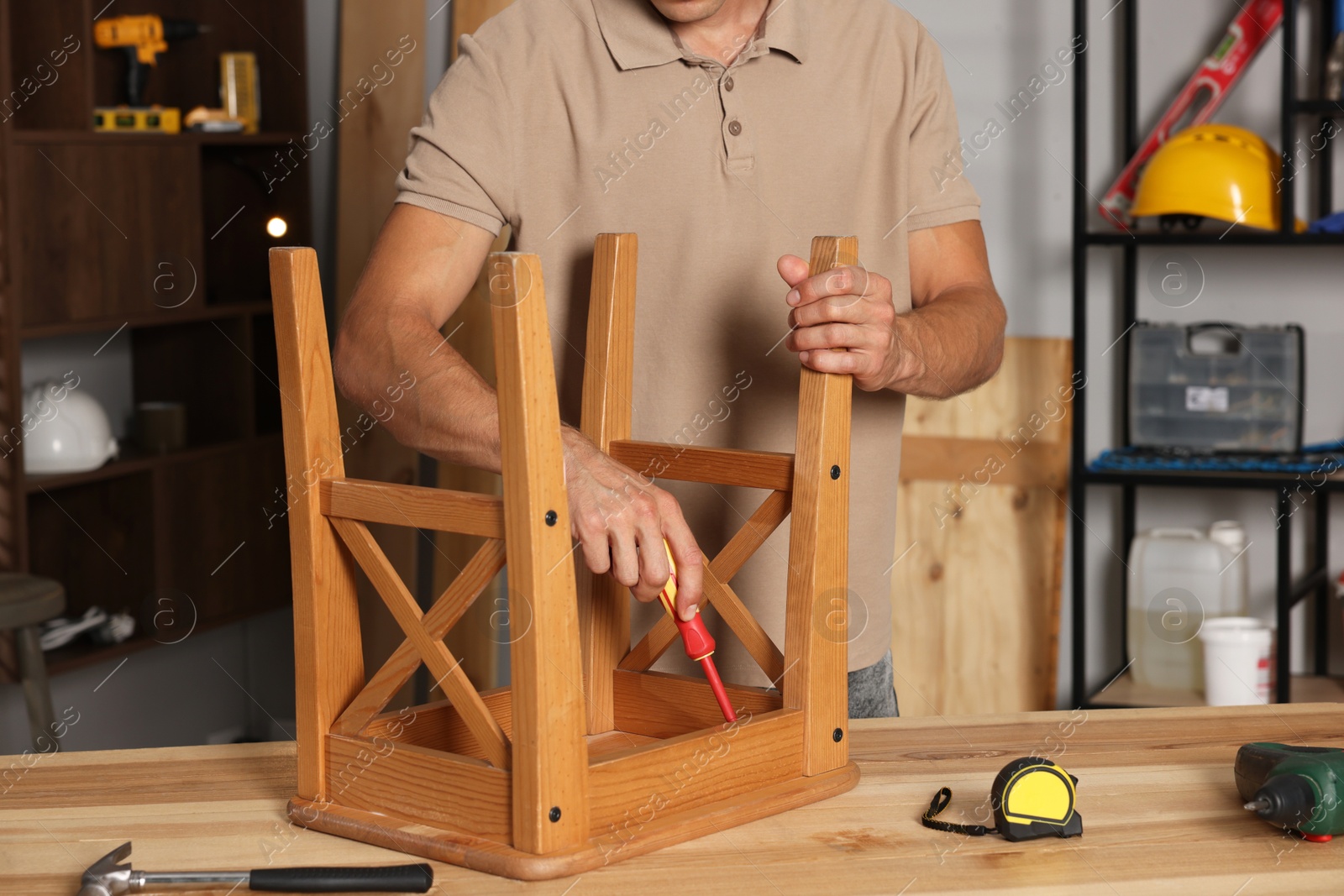 Photo of Man repairing wooden stool with screwdriver indoors, closeup