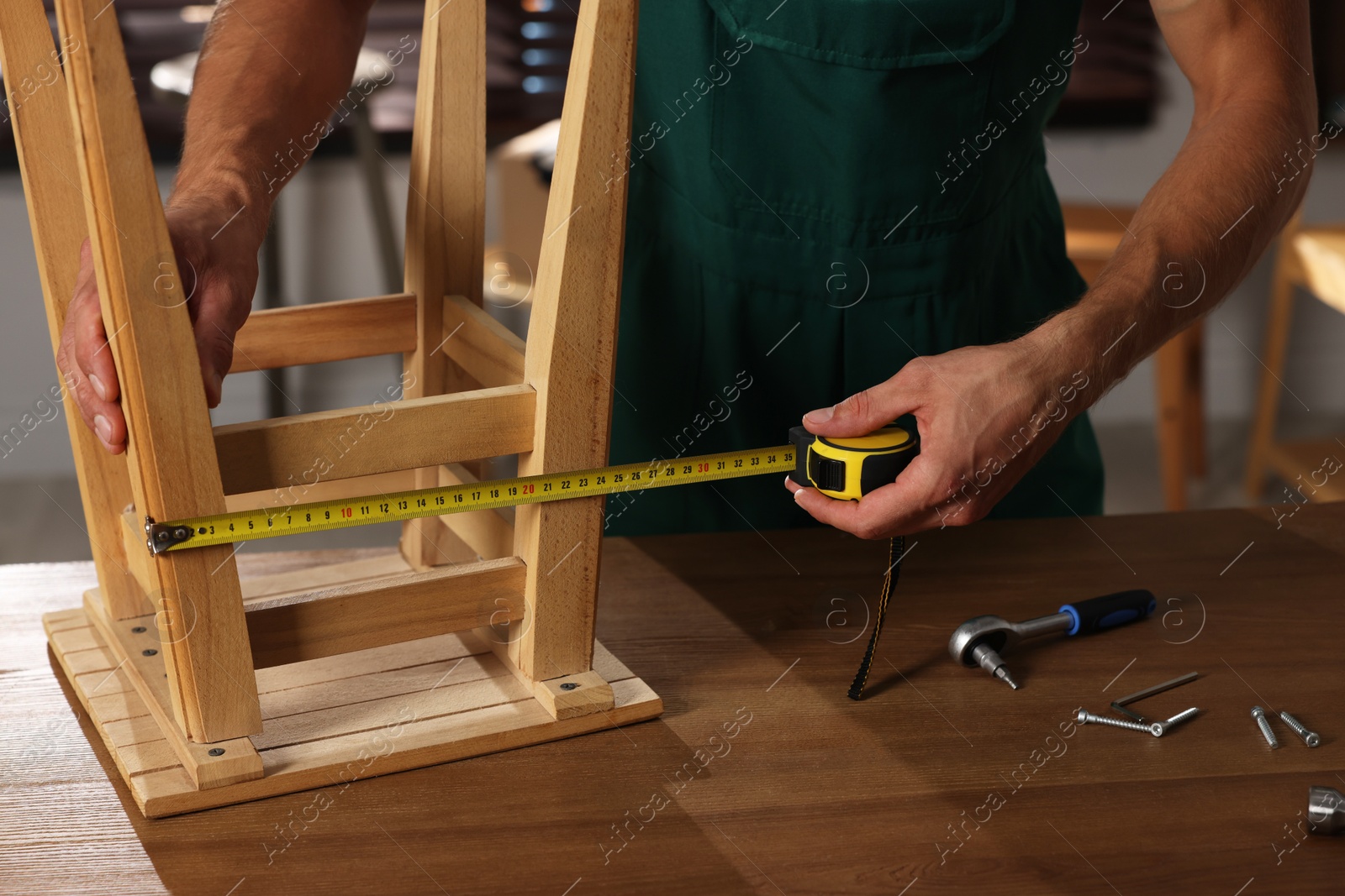 Photo of Man using tape measure while repairing wooden stool indoors, closeup