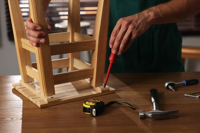 Photo of Man repairing wooden stool with screwdriver indoors, closeup