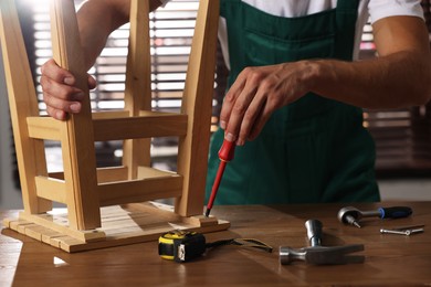 Man repairing wooden stool with screwdriver indoors, closeup