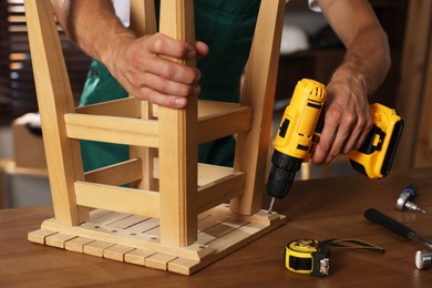 Man repairing wooden stool with electric screwdriver indoors, closeup