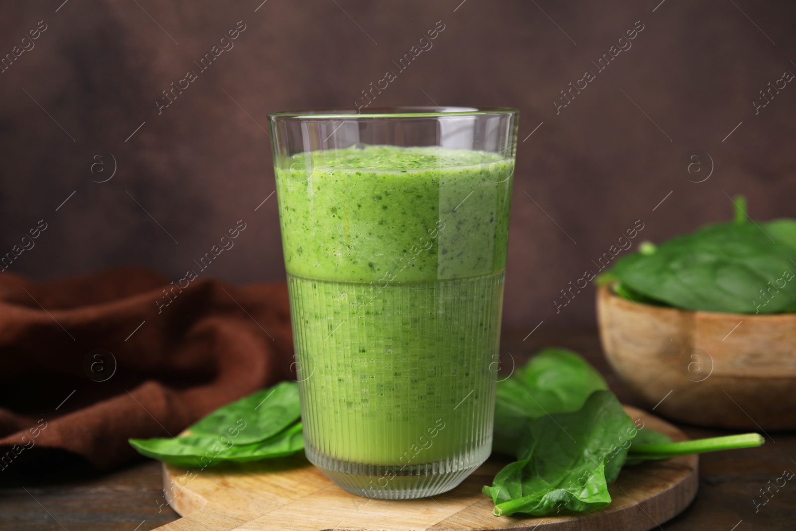 Photo of Tasty green smoothie in glass and spinach on wooden table, closeup