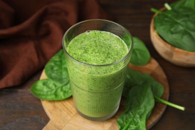 Photo of Tasty green smoothie in glass and spinach on wooden table, closeup