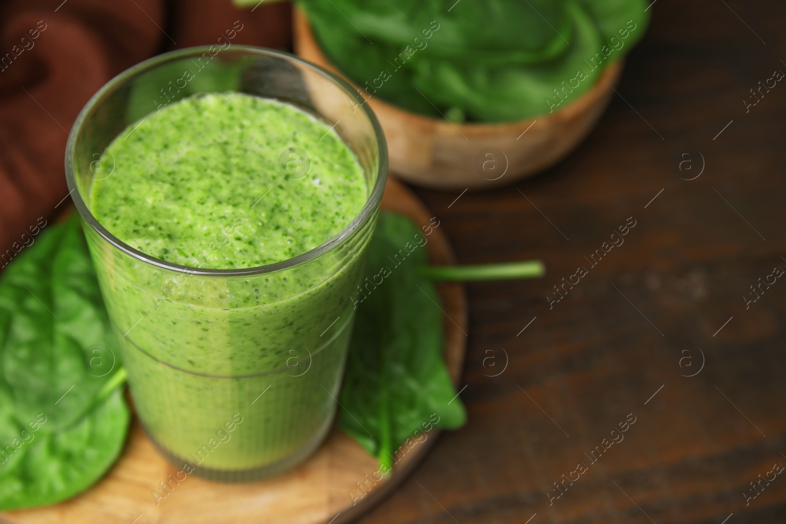 Photo of Tasty green smoothie in glass and spinach on wooden table, closeup. Space for text