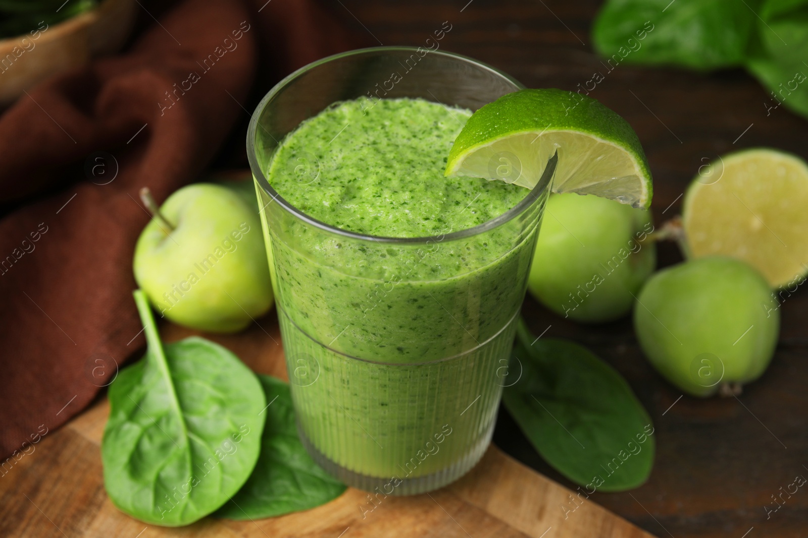 Photo of Tasty green smoothie in glass with lime, apples and spinach on wooden table, closeup