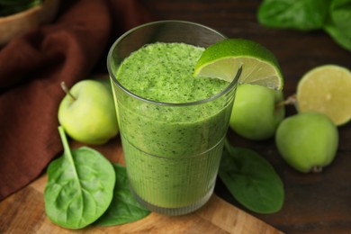 Photo of Tasty green smoothie in glass with lime, apples and spinach on wooden table, closeup