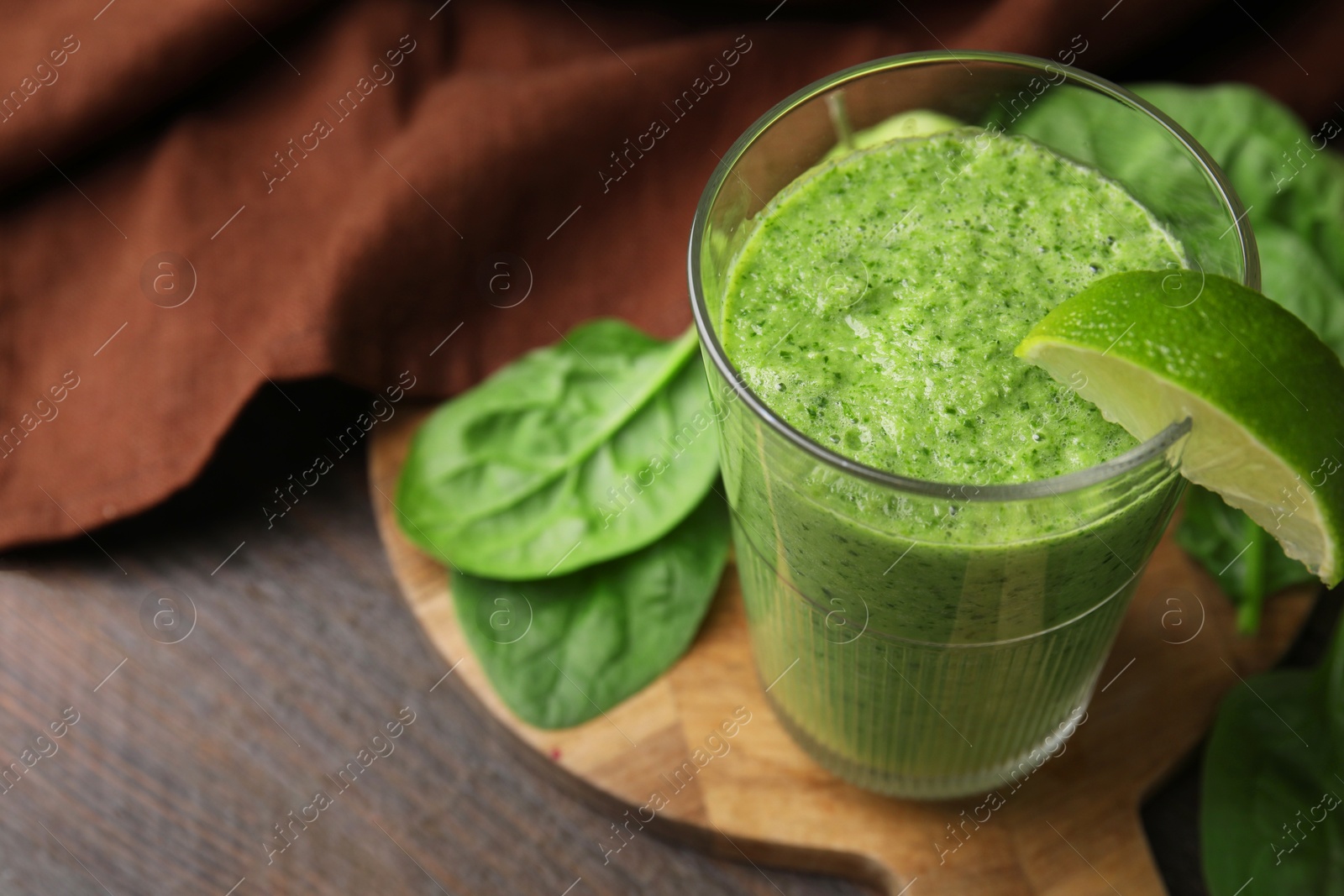 Photo of Tasty green smoothie in glass with lime and spinach on wooden table, closeup. Space for text