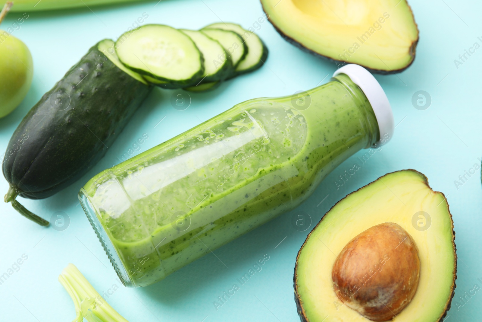 Photo of Tasty green smoothie in bottle and products on light blue background, closeup