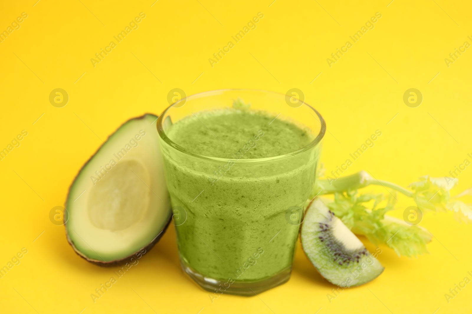 Photo of Delicious green smoothie and ingredients on yellow table, closeup