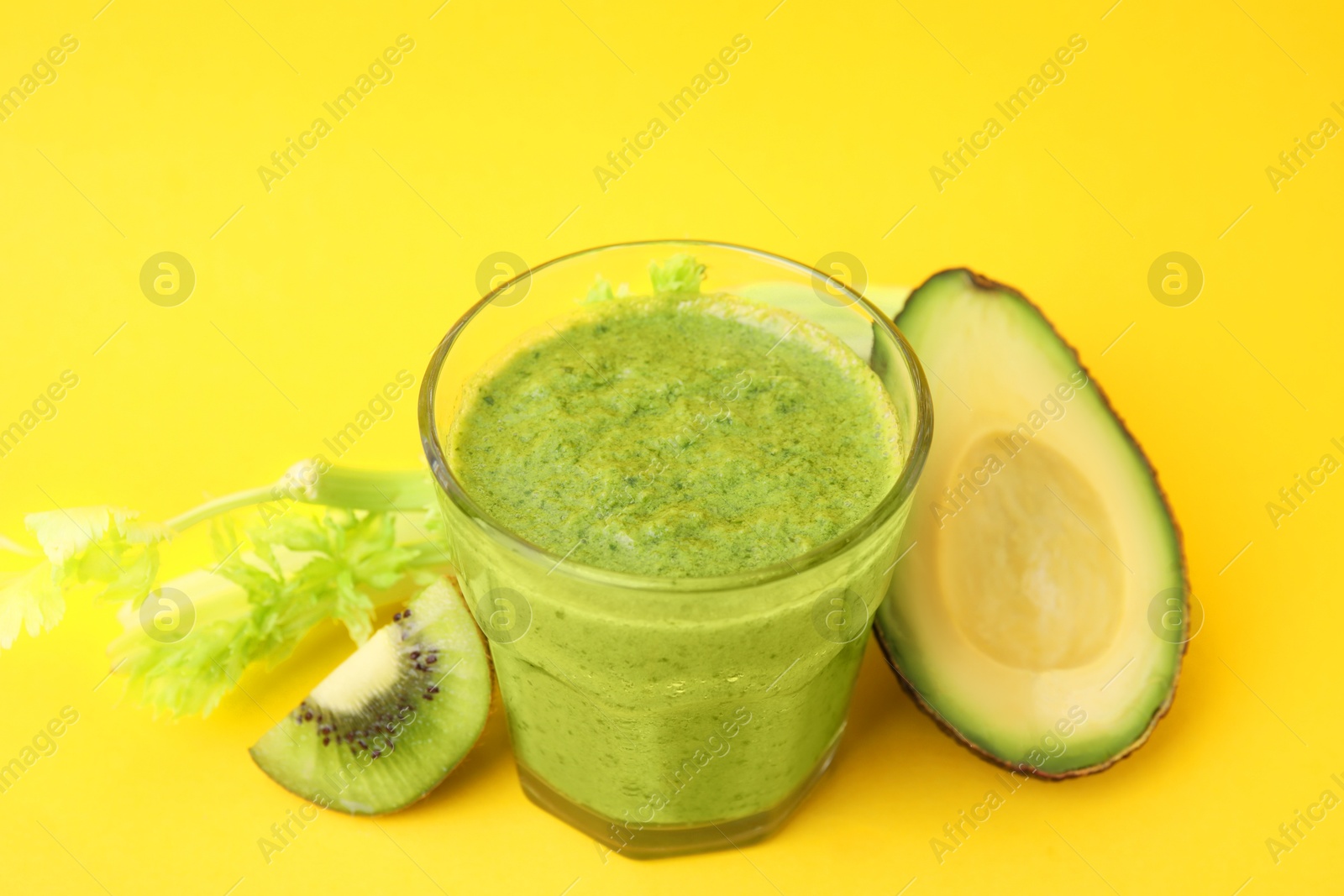 Photo of Delicious green smoothie and ingredients on yellow table, closeup