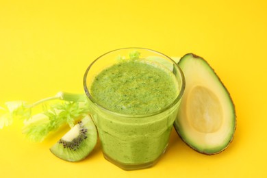 Photo of Delicious green smoothie and ingredients on yellow table, closeup