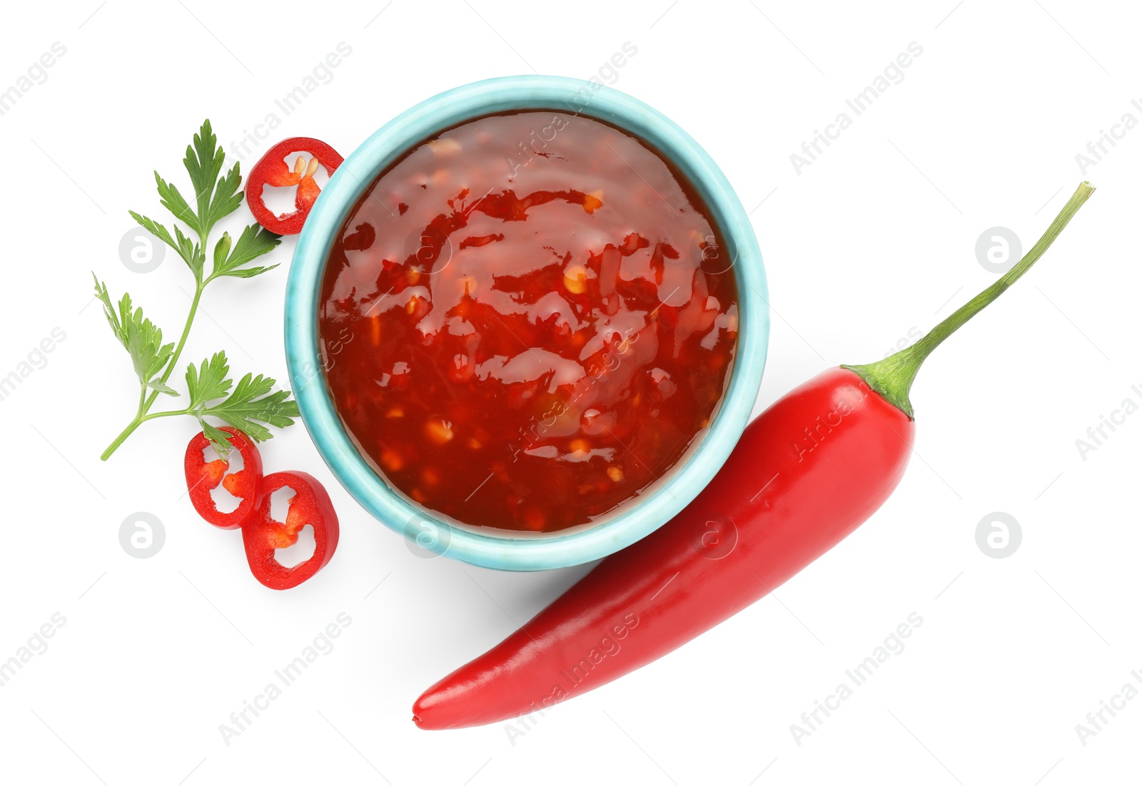 Photo of Hot chili sauce in bowl, parsley and pepper isolated on white, top view