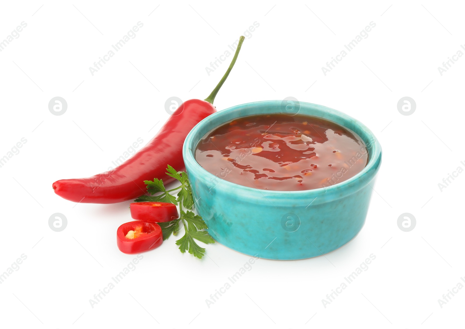 Photo of Hot chili sauce in bowl, parsley and pepper isolated on white