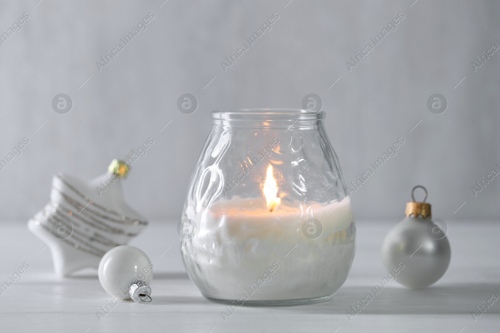 Photo of Burning candle and baubles on white wooden table, closeup