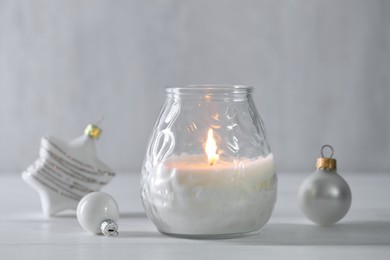 Photo of Burning candle and baubles on white wooden table, closeup