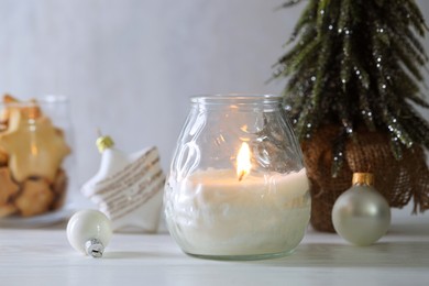 Photo of Burning candle and Christmas decor on white wooden table, closeup