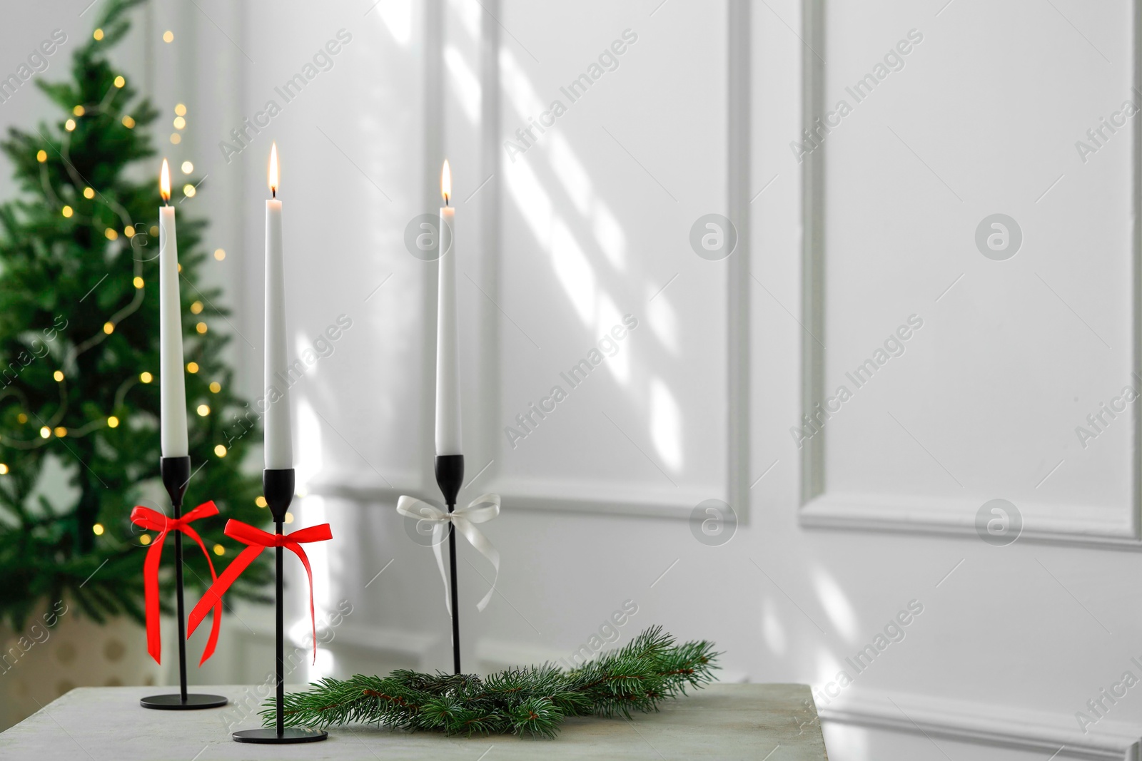 Photo of Burning candles on white table and Christmas tree at home, space for text