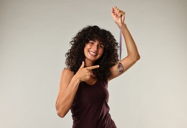 Happy winner pointing at bronze medal on light grey background