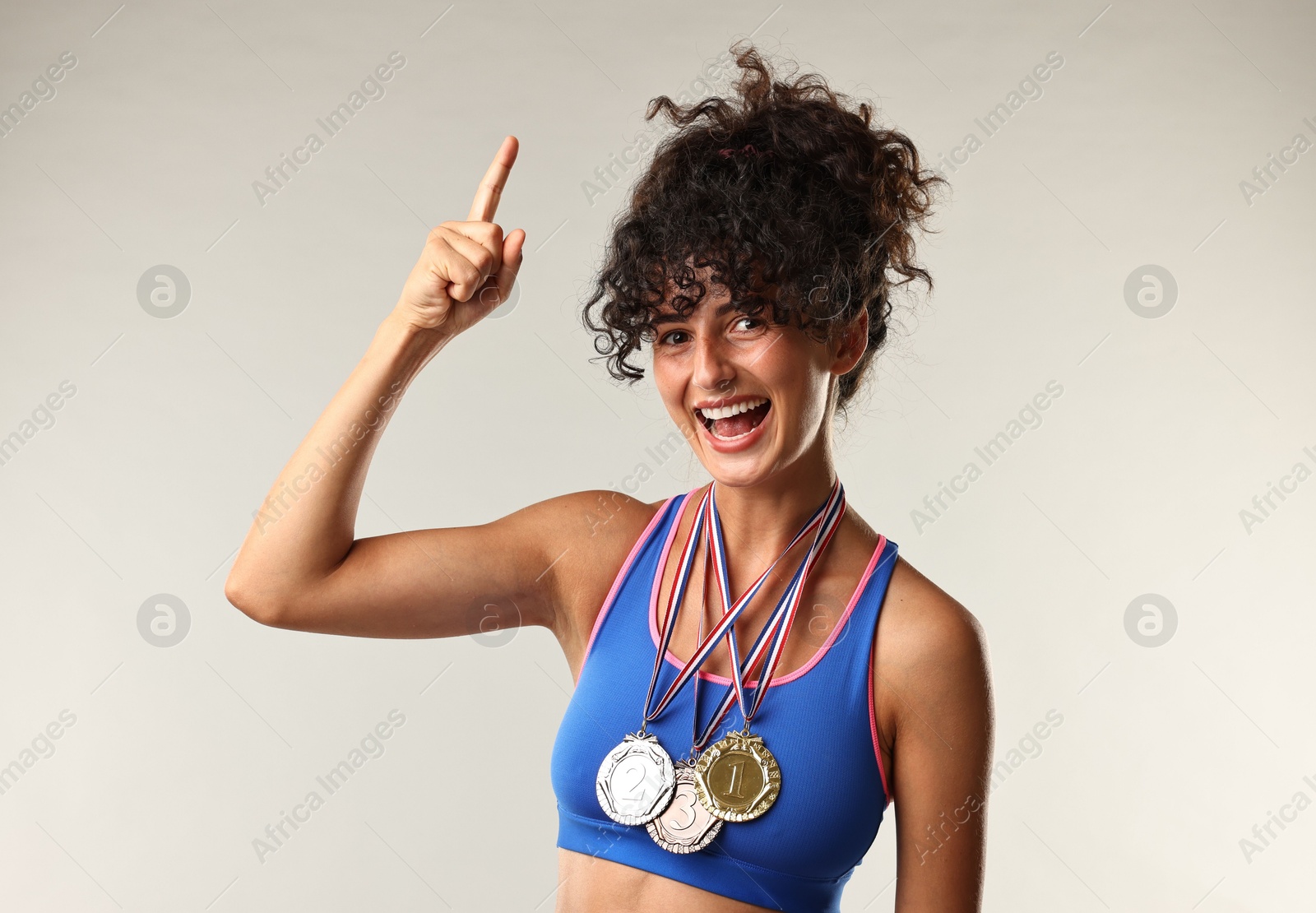 Photo of Happy winner with different medals pointing upwards on light grey background