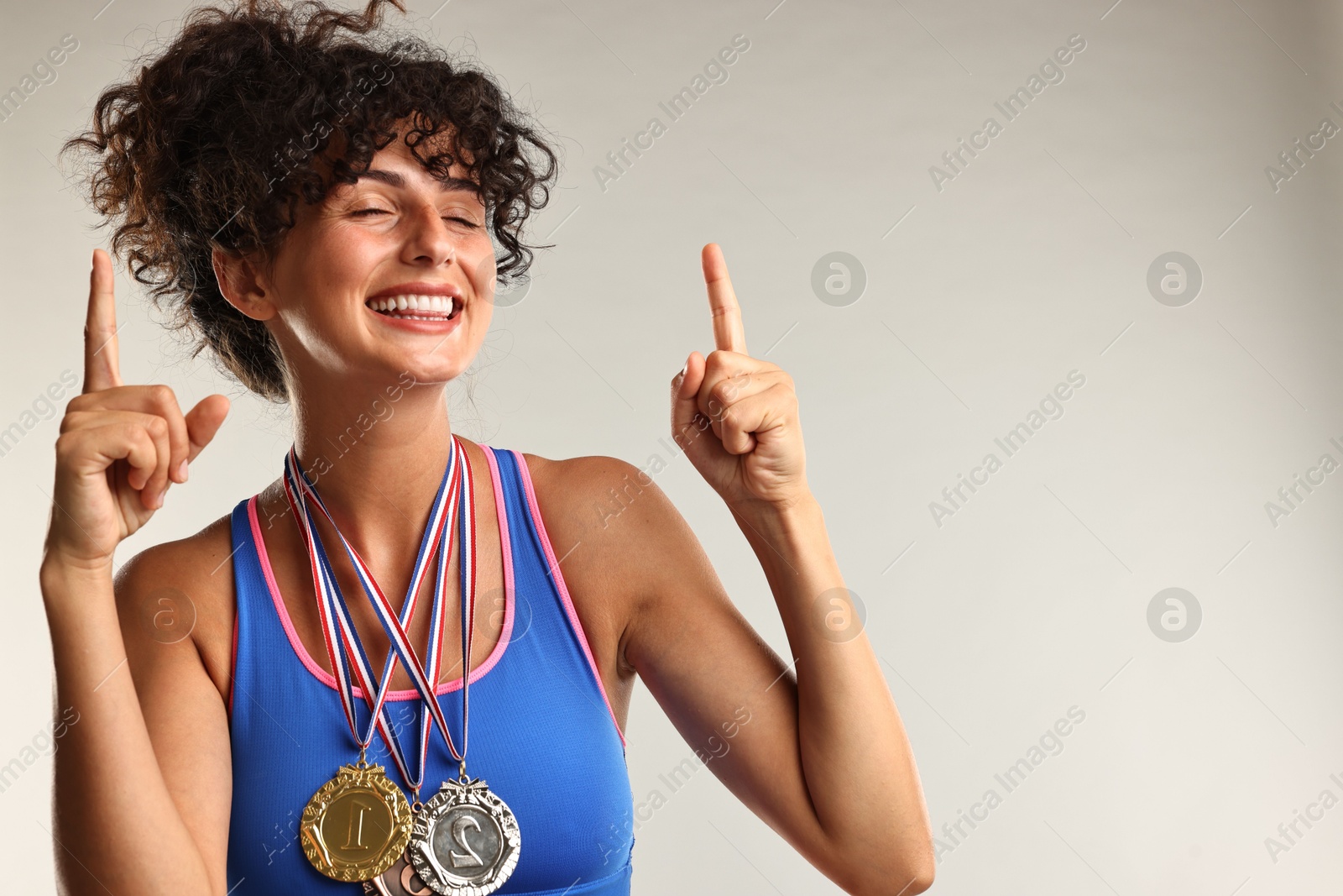 Photo of Happy winner with different medals pointing upwards on light grey background. Space for text