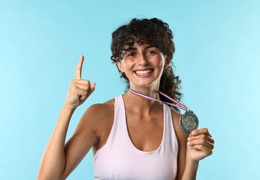 Photo of Happy winner with silver medal pointing upwards on light blue background