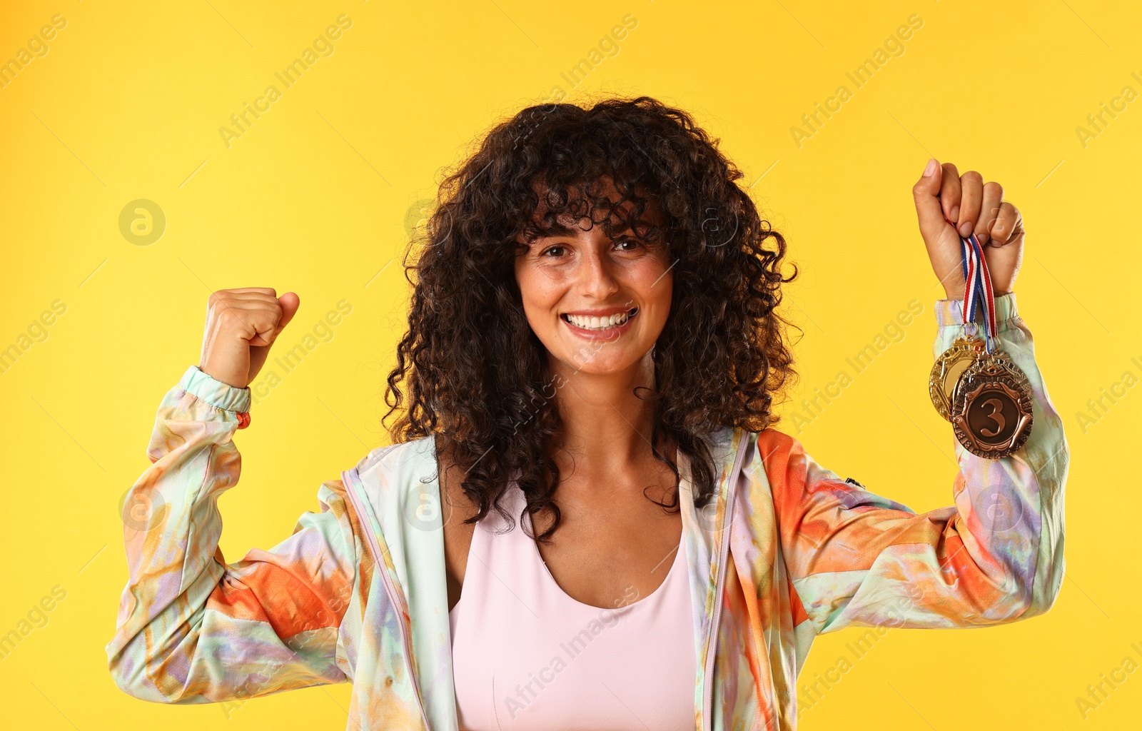 Photo of Happy winner showing different medals on yellow background