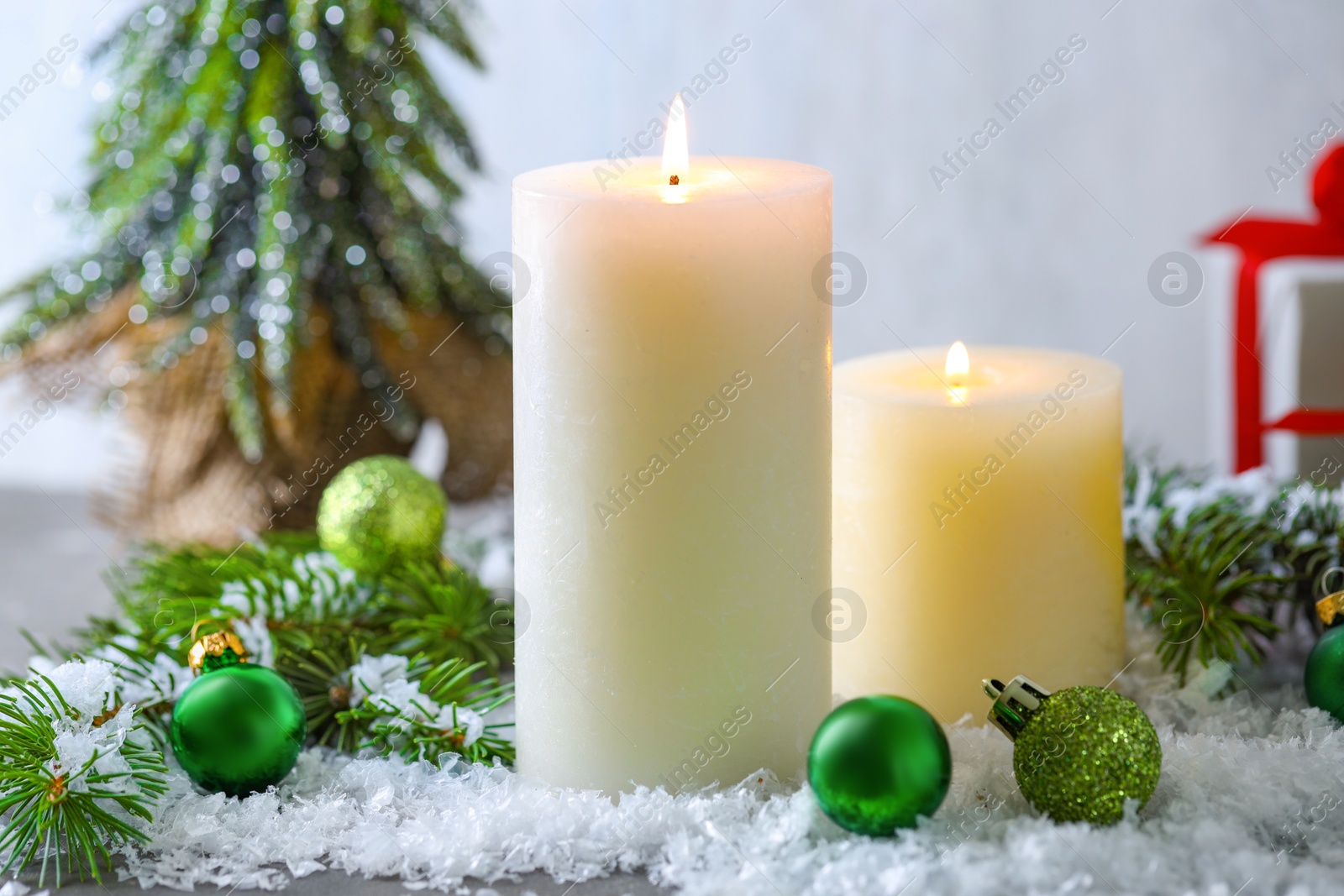 Photo of Burning candles, baubles and fir branches on artificial snow, closeup. Christmas atmosphere