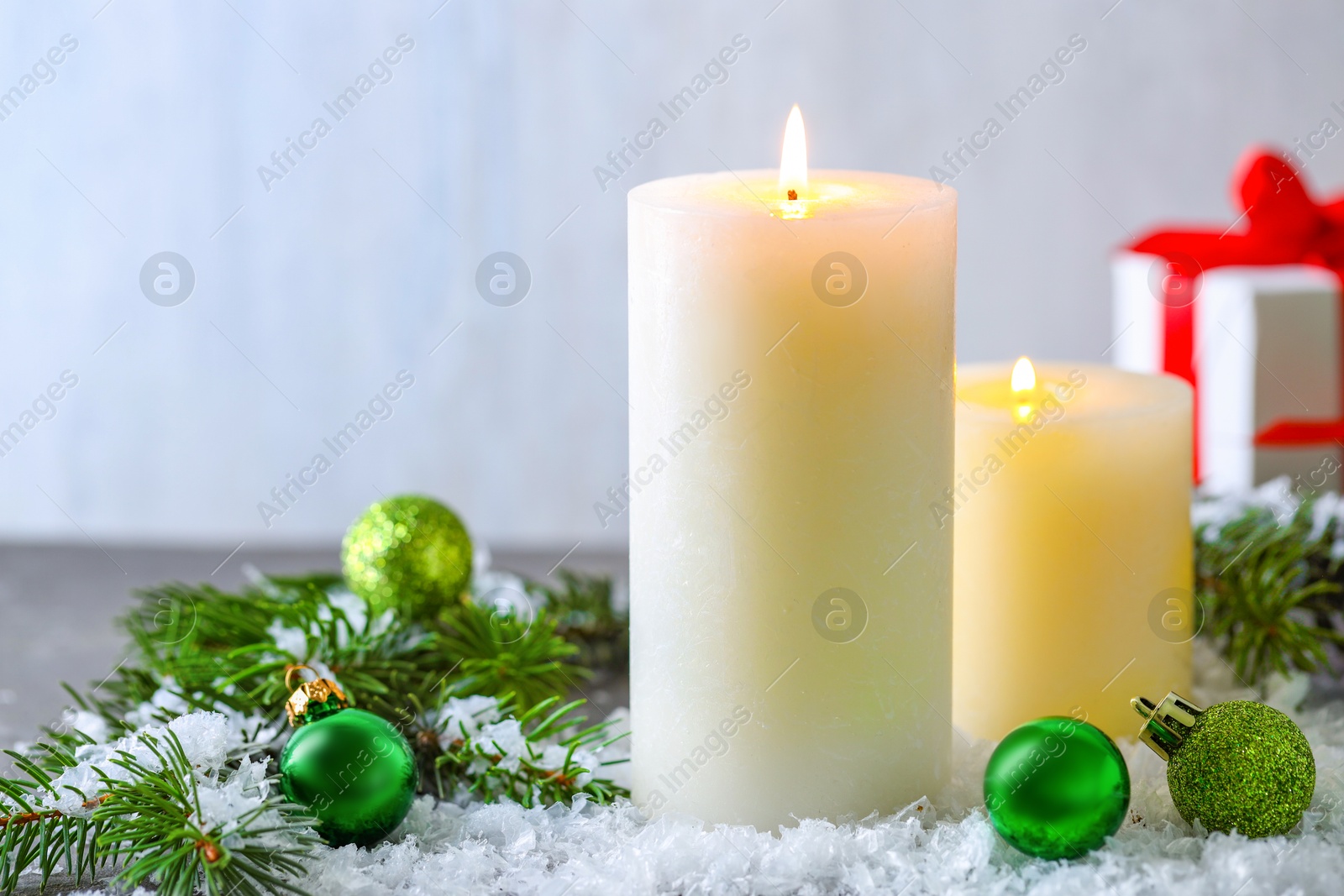 Photo of Burning candles, baubles and fir branches on artificial snow, closeup. Christmas atmosphere