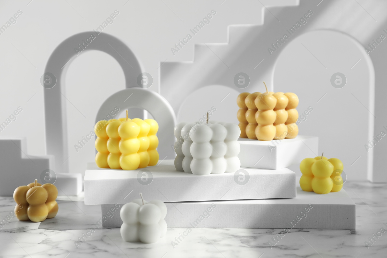 Photo of Beautiful bubble candles and geometric figures on white marble table