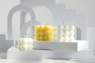 Photo of Beautiful bubble candles and geometric figures on white marble table