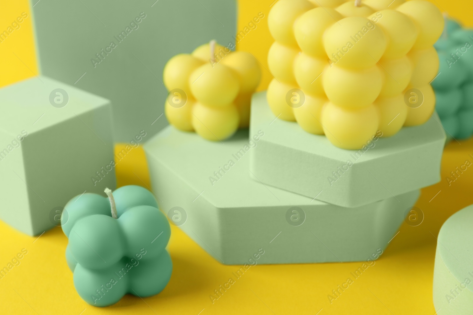 Photo of Beautiful bubble candles and podiums on yellow background, closeup