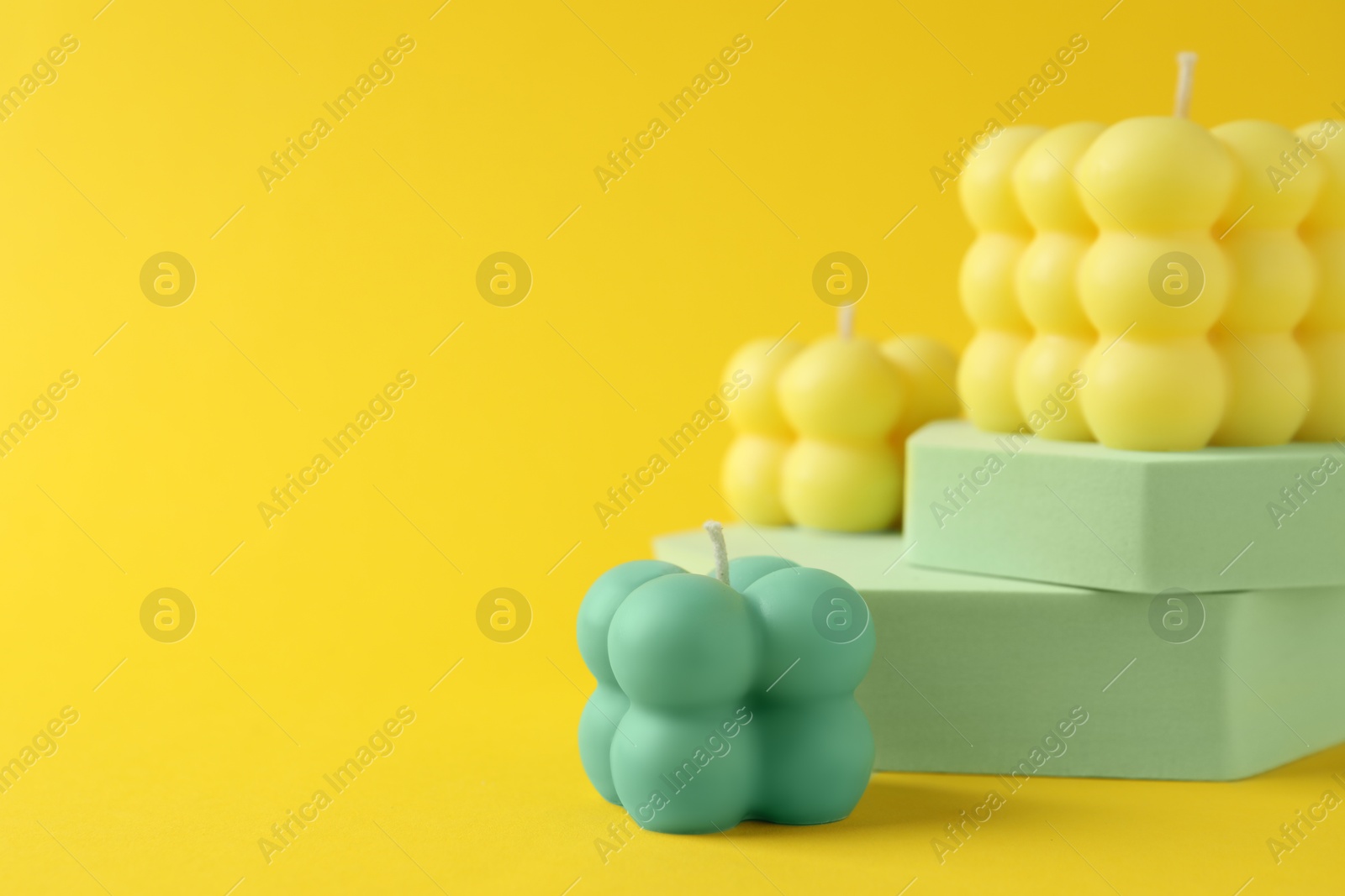 Photo of Beautiful bubble candles and podiums on yellow background, space for text