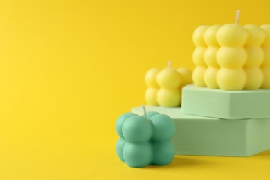 Photo of Beautiful bubble candles and podiums on yellow background, space for text