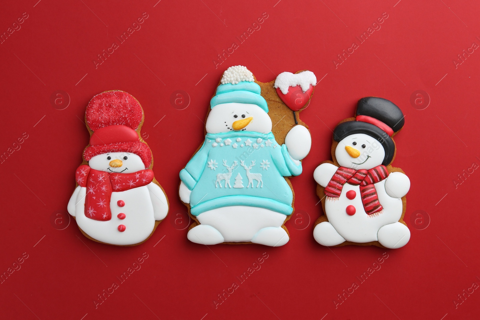 Photo of Tasty Christmas cookies in shape of snowman on red background, flat lay