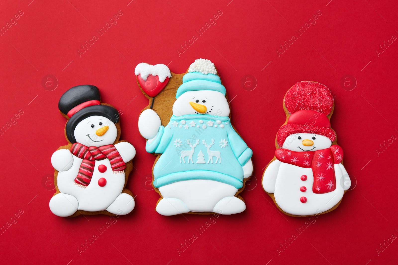 Photo of Tasty Christmas cookies in shape of snowman on red background, flat lay