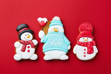 Photo of Tasty Christmas cookies in shape of snowman on red background, flat lay