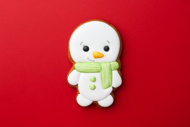 Photo of Tasty Christmas cookie in shape of snowman on red background, top view