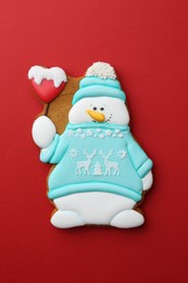 Photo of Tasty Christmas cookie in shape of snowman on red background, top view