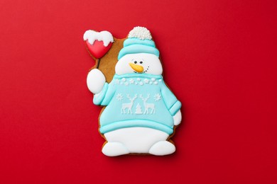 Tasty Christmas cookie in shape of snowman on red background, top view